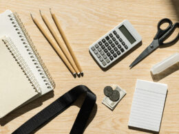 Flat lay of back to school supplies with notebooks, pencils, calculator and cash on light wood