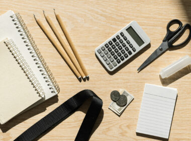 Flat lay of back to school supplies with notebooks, pencils, calculator and cash on light wood