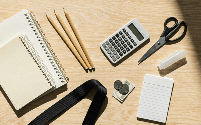 Flat lay of back to school supplies with notebooks, pencils, calculator and cash on light wood
