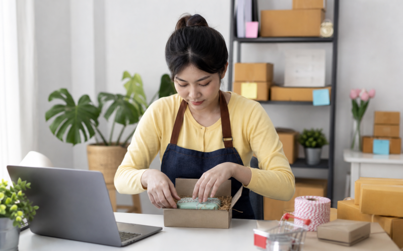 A person packing small handmade products for shipping at a home desk