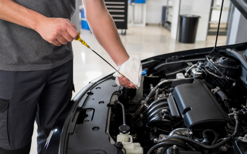 A person checking the oil dipstick in an open car engine bay