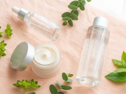 Dewy glass skin skincare products with a serum dropper, cream jar, and fresh green leaves