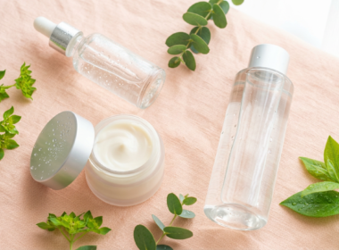 Dewy glass skin skincare products with a serum dropper, cream jar, and fresh green leaves