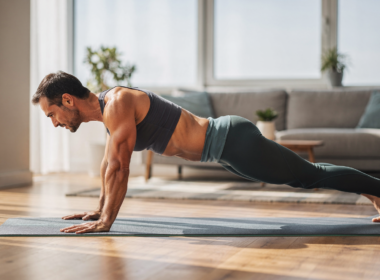 A person holding a plank on a yoga mat in a bright living room