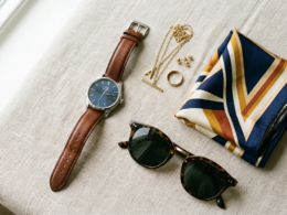 Fashion accessories including a watch, sunglasses, scarf, and jewelry on a surface