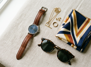 Fashion accessories including a watch, sunglasses, scarf, and jewelry on a surface
