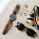 Fashion accessories including a watch, sunglasses, scarf, and jewelry on a surface