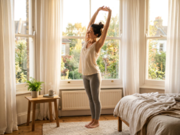 A person stretching by a sunlit window with open curtains