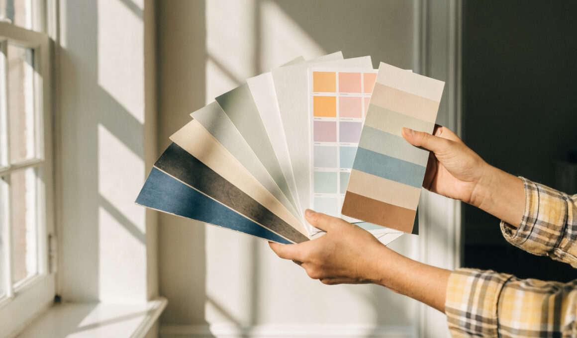 Paint color swatches held against a wall in a bright room