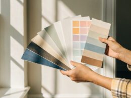 Paint color swatches held against a wall in a bright room