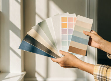 Paint color swatches held against a wall in a bright room