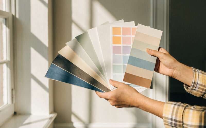 Paint color swatches held against a wall in a bright room
