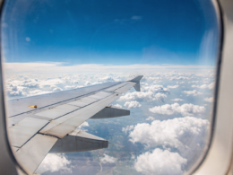 View of an airplane wing over blue sky and clouds through a cabin window