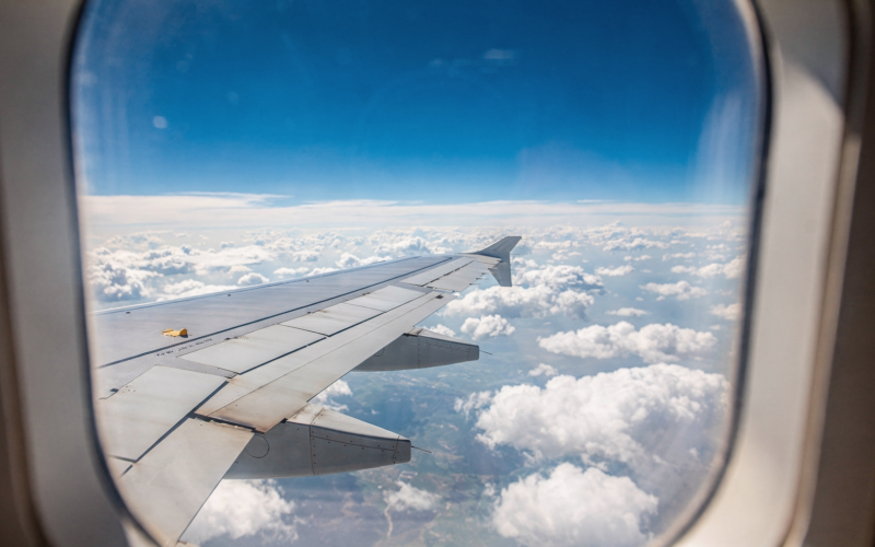 View of an airplane wing over blue sky and clouds through a cabin window