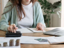 A person budgeting at a desk with a calculator, notebook, and laptop
