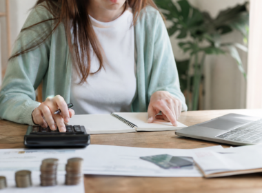 A person budgeting at a desk with a calculator, notebook, and laptop