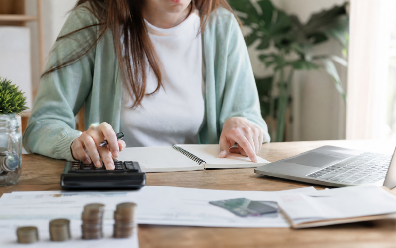 A person budgeting at a desk with a calculator, notebook, and laptop