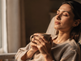 A person relaxing with eyes closed by a window holding a warm drink