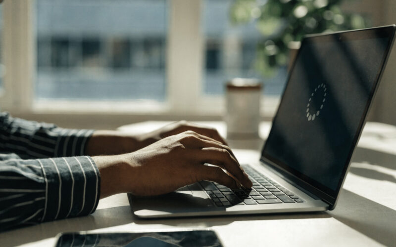 Hands on a laptop keyboard with a loading spinner on screen while troubleshooting a slow computer