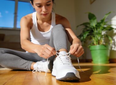 A person in workout clothes lacing up their sneakers at home