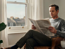 A person calmly reading a newspaper with coffee by a window