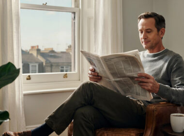 A person calmly reading a newspaper with coffee by a window
