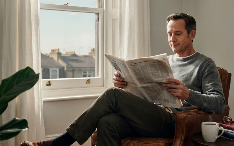 A person calmly reading a newspaper with coffee by a window