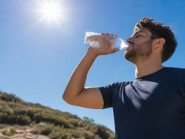 A person drinking water outdoors under a bright hot sun