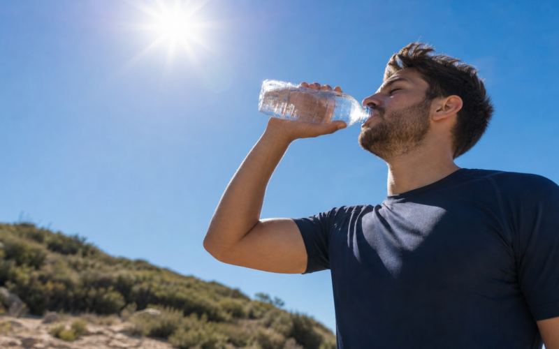 A person drinking water outdoors under a bright hot sun