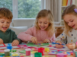 Happy young children doing arts and crafts at a table indoors on a rainy day
