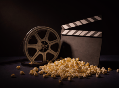 A film reel, clapperboard, and popcorn arranged on a dark surface