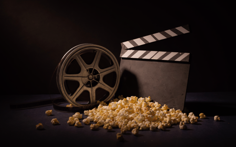 A film reel, clapperboard, and popcorn arranged on a dark surface