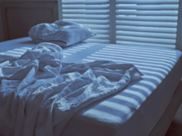 Unmade bed at dawn with light coming through window blinds