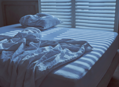 Unmade bed at dawn with light coming through window blinds