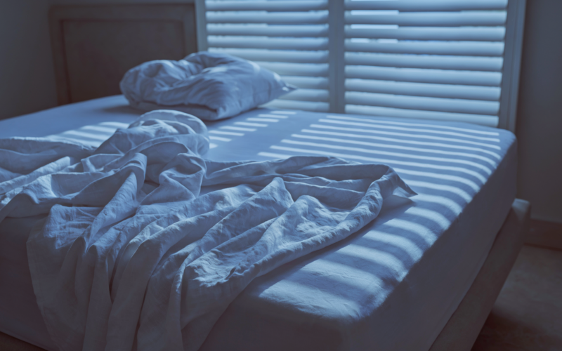 Unmade bed at dawn with light coming through window blinds