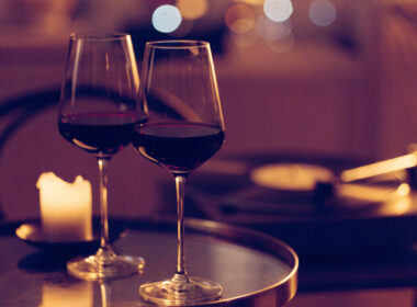 Two glasses of red wine, a glowing candle, and a vinyl record player in warm evening light