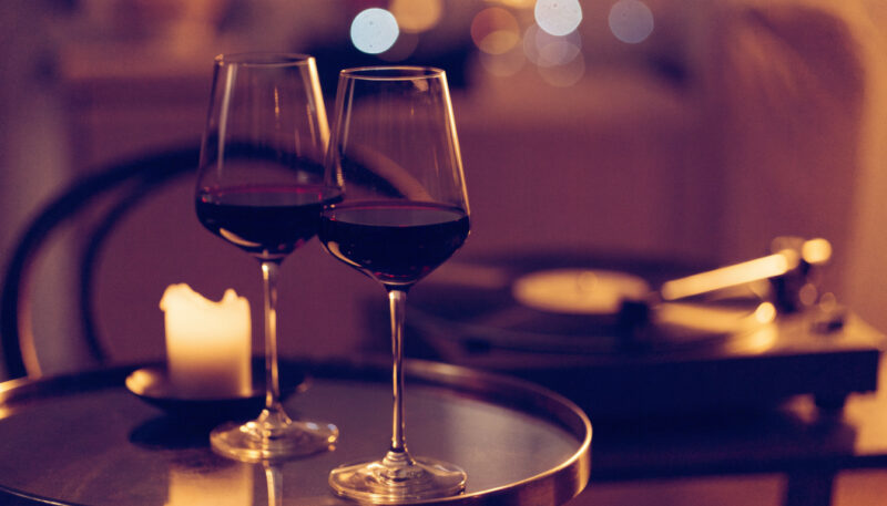 Two glasses of red wine, a glowing candle, and a vinyl record player in warm evening light