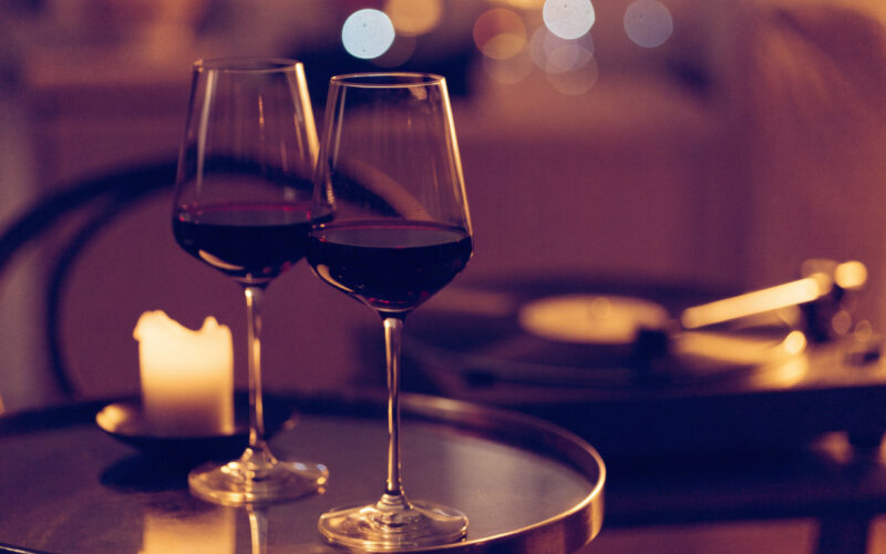 Two glasses of red wine, a glowing candle, and a vinyl record player in warm evening light