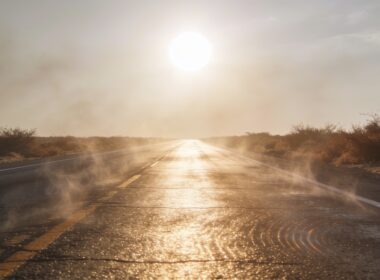 Heat haze rising off an empty rural highway under a blazing midsummer sun