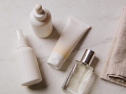 Sunscreen, skincare bottles and a perfume flacon arranged on a pale marble surface