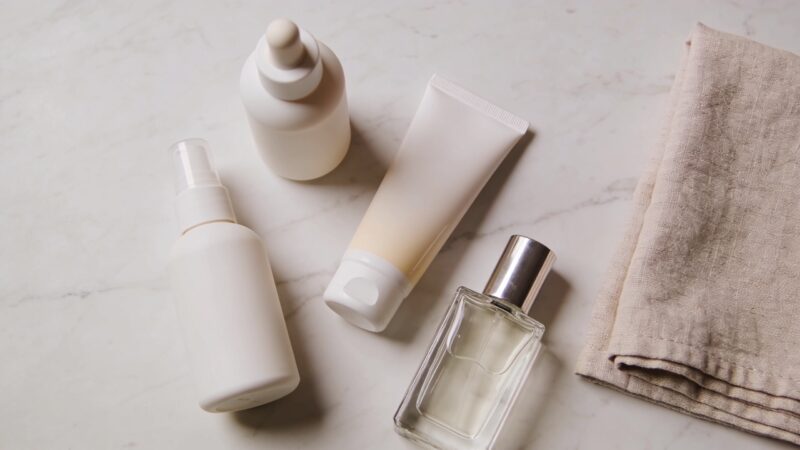 Sunscreen, skincare bottles and a perfume flacon arranged on a pale marble surface