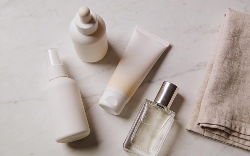 Sunscreen, skincare bottles and a perfume flacon arranged on a pale marble surface