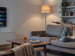 A person on a couch pointing a TV remote at a television