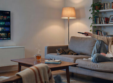 A person on a couch pointing a TV remote at a television