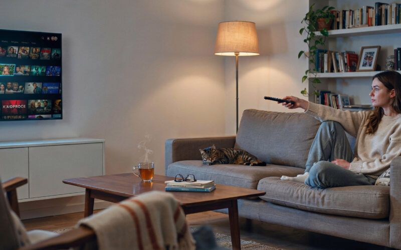 A person on a couch pointing a TV remote at a television
