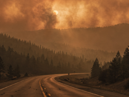 Wildfire smoke drifting over forested ridges above an empty closed highway