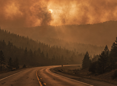 Wildfire smoke drifting over forested ridges above an empty closed highway