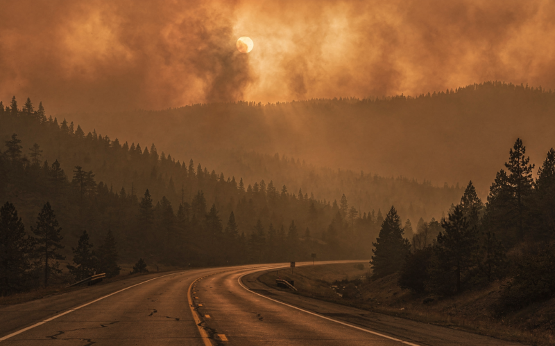 Wildfire smoke drifting over forested ridges above an empty closed highway