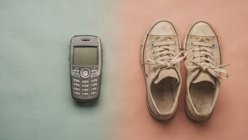 A retro smartphone and vintage sneakers arranged on a split colored surface blending two eras