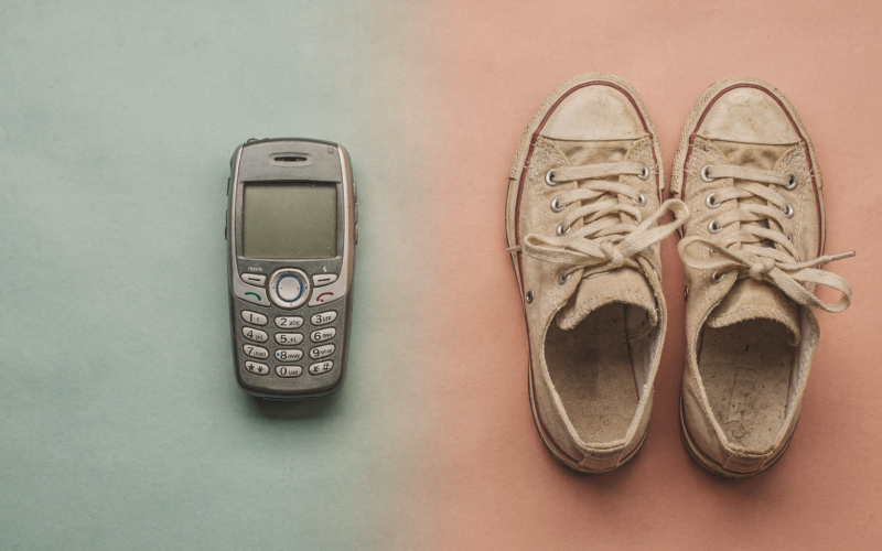 A retro smartphone and vintage sneakers arranged on a split colored surface blending two eras